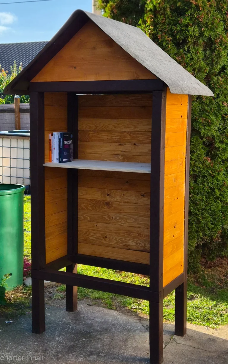 Einige Bücher stehen auf dem ersten Einlegeboden des noch türlosen Bücherhauses mit honigfarbener Holzverkleidung.