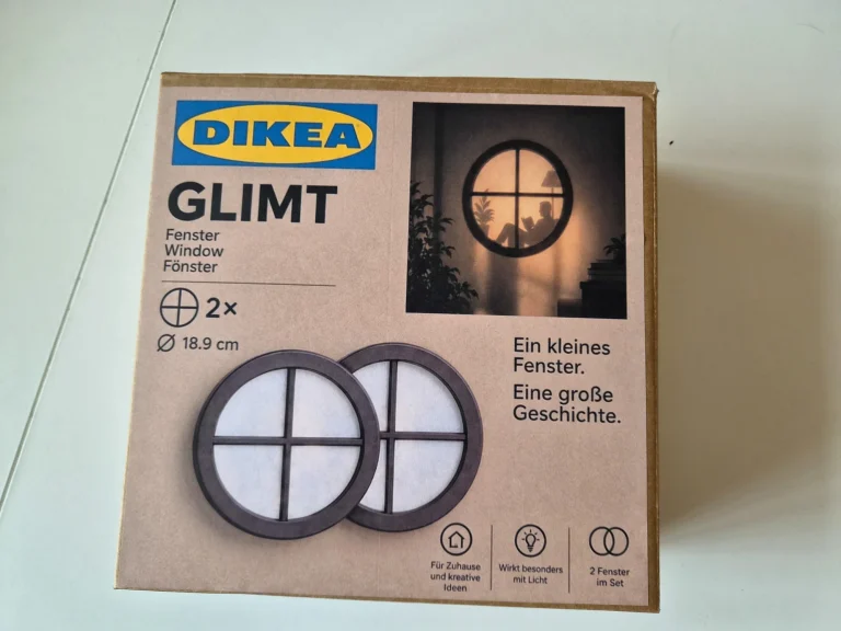 Selbst gestaltete Verpackung mit der Aufschrift „DIKEA GLIMT“ und Abbildungen der runden Giebelfenster samt beleuchtetem Lesemotiv.